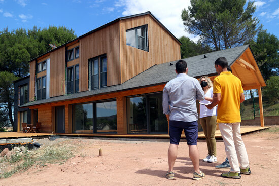 A wooden house in Bages with the owners and construction company officials standing in front of it (by Nia Escolà)